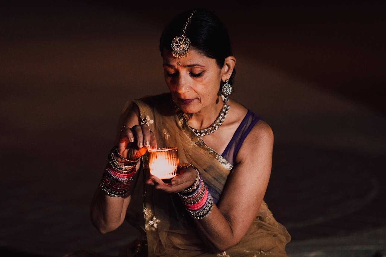 A senior Indian woman in traditional clothing holding a lit candle during Diwali.
